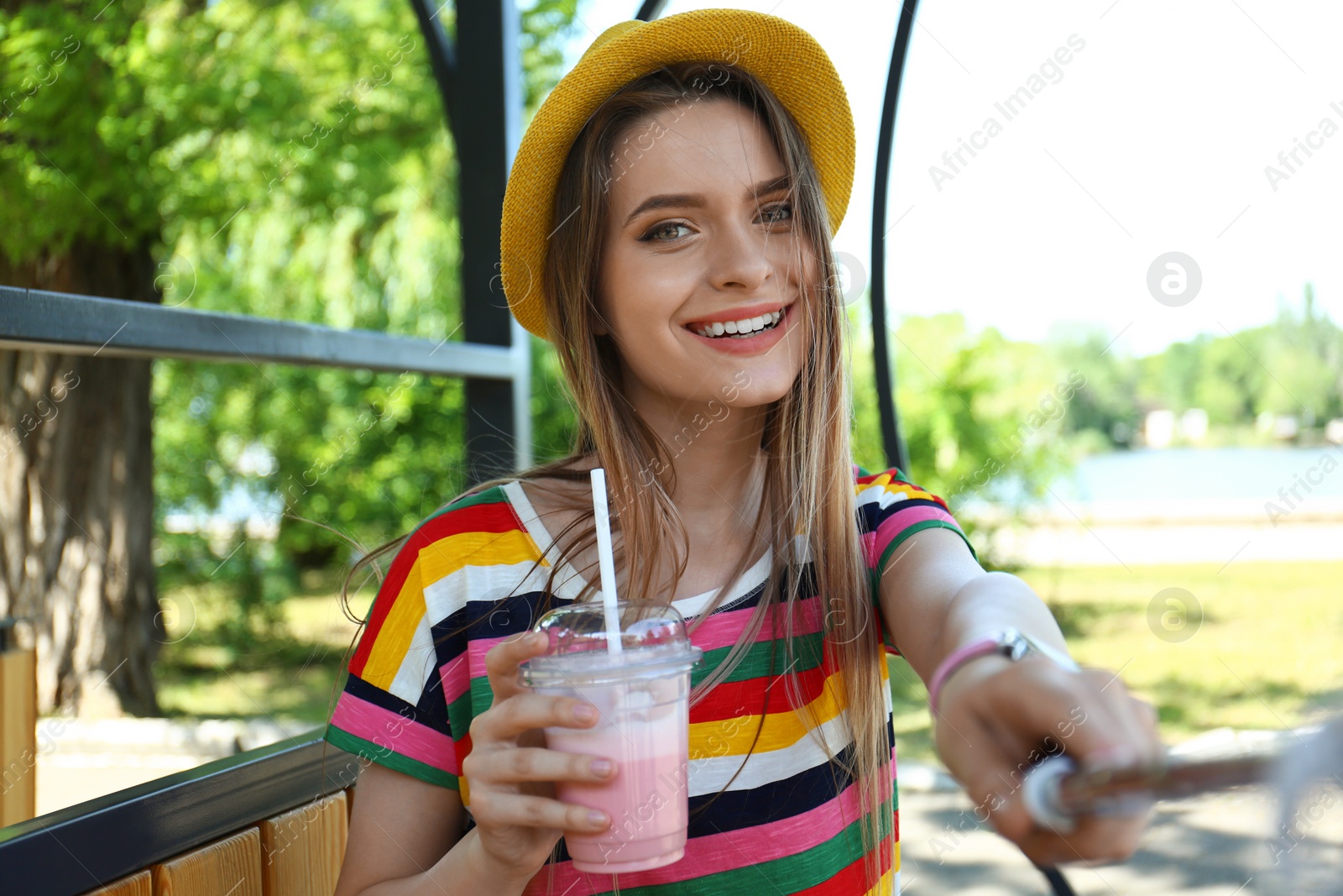 Photo of Happy young woman with drink taking selfie in park