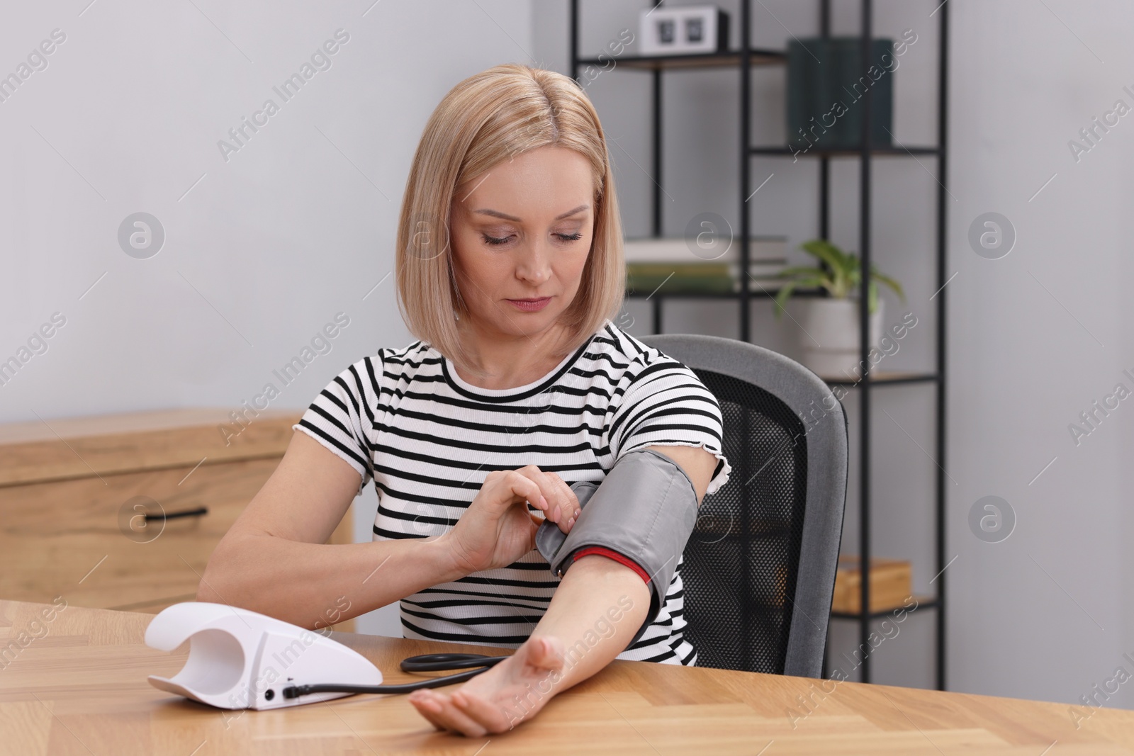 Photo of Woman measuring her blood pressure with tonometer at wooden table indoors