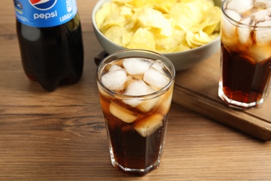 Photo of MYKOLAIV, UKRAINE - FEBRUARY 15, 2021: Glasses and bottle of Pepsi on wooden table