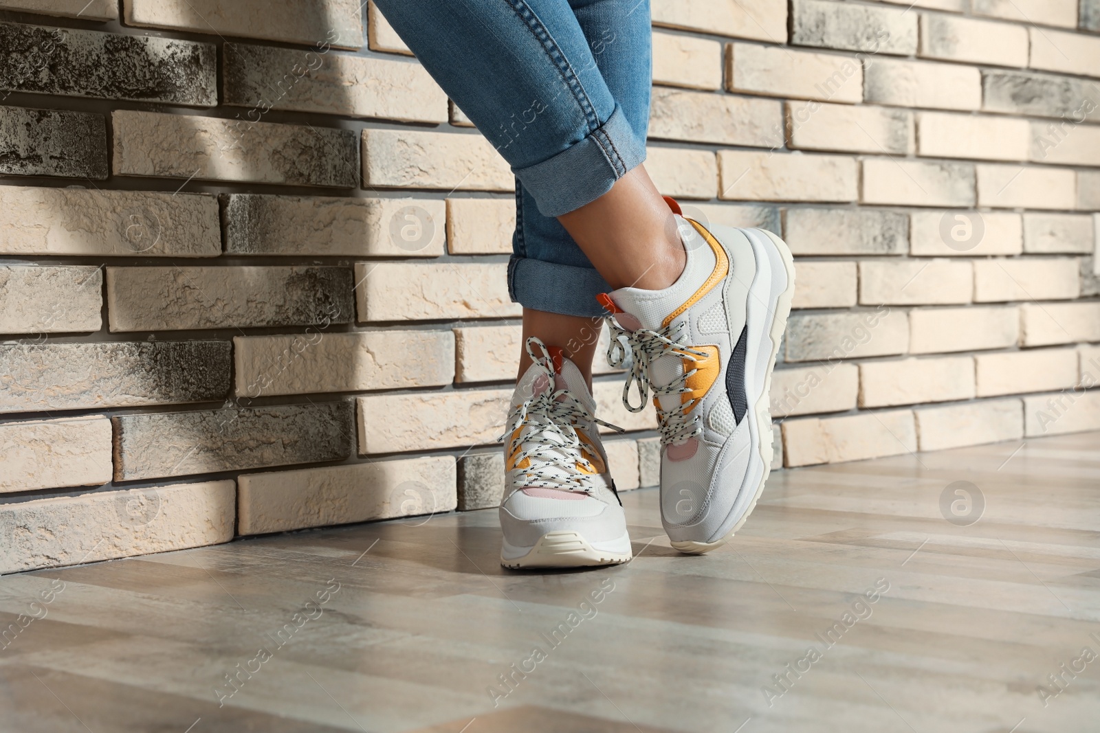 Photo of Woman in stylish sneakers near brick wall indoors, closeup