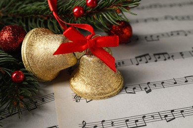 Photo of Golden shiny bells and fir branches with Christmas decor on music sheets, closeup. Space for text