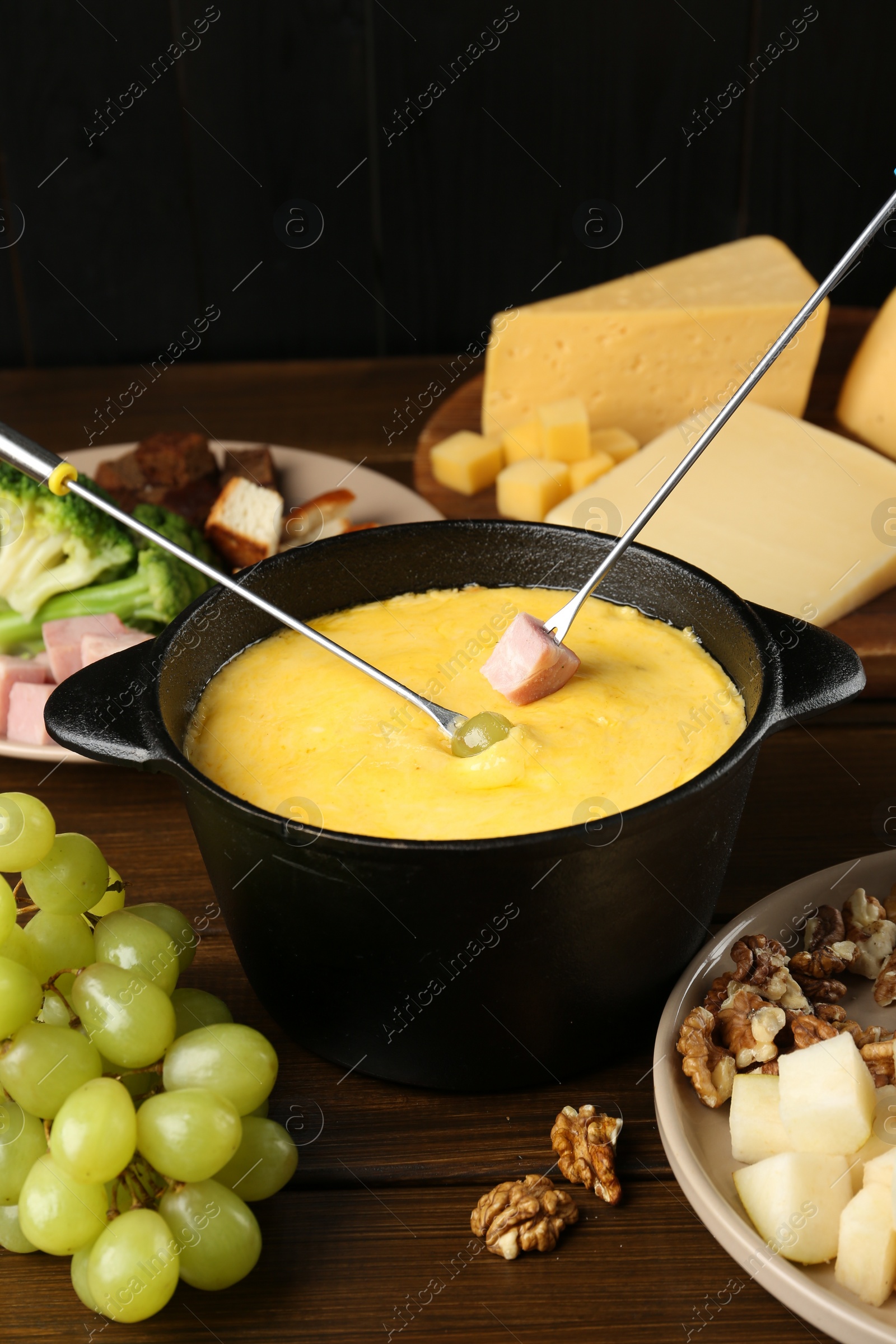 Photo of Fondue pot with melted cheese, forks and different products on wooden table