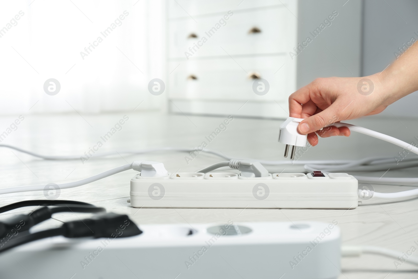 Photo of Woman inserting power plug into extension cord on floor indoors, closeup with space for text. Electrician's professional equipment