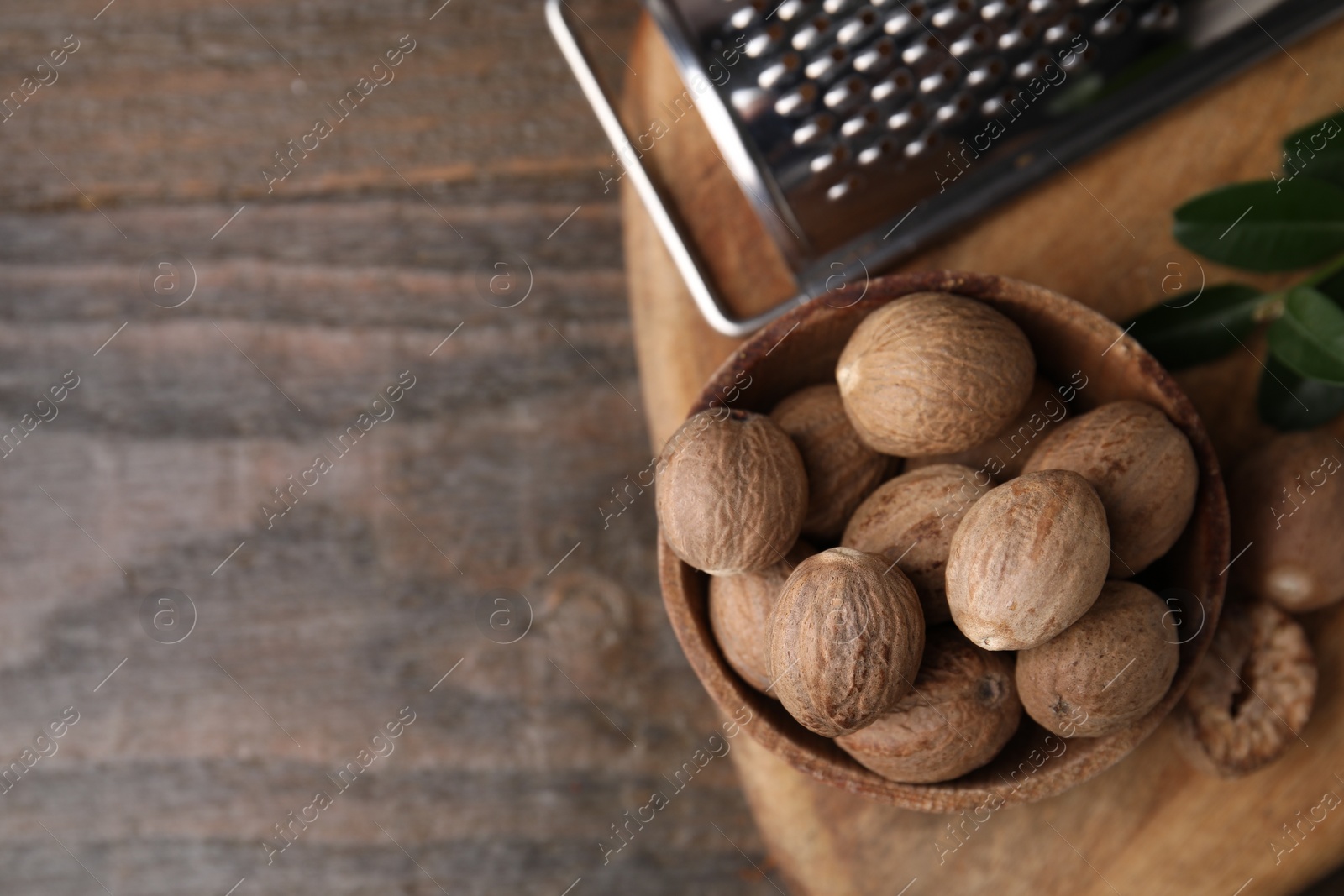 Photo of Nutmegs in bowl and grater on wooden table, flat lay. Space for text