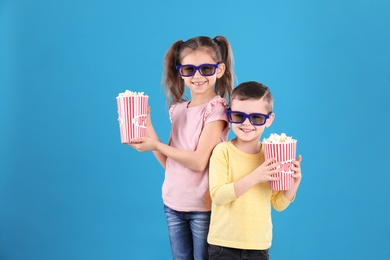 Cute children with popcorn and glasses on color background