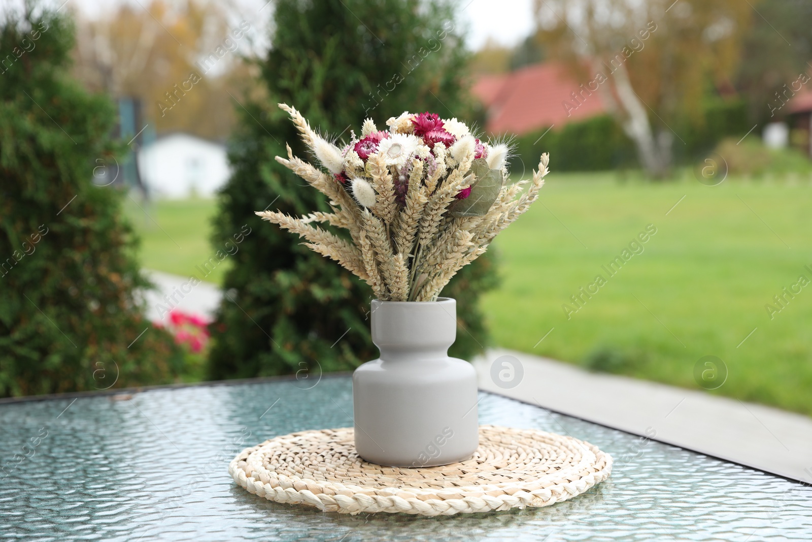 Photo of Beautiful bouquet of dry flowers in vase on glass table outdoors