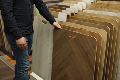 Man choosing wooden flooring among different samples in shop, closeup