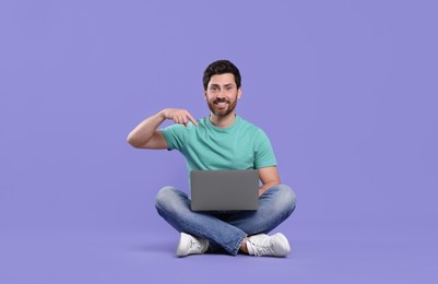Happy man with laptop on purple background