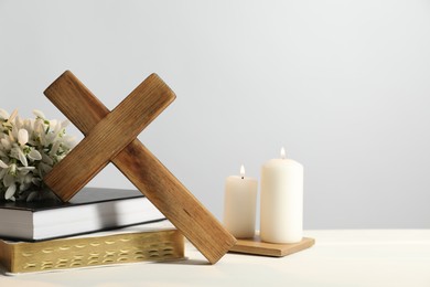 Burning church candles, wooden cross, ecclesiastical books and flowers on white table. Space for text