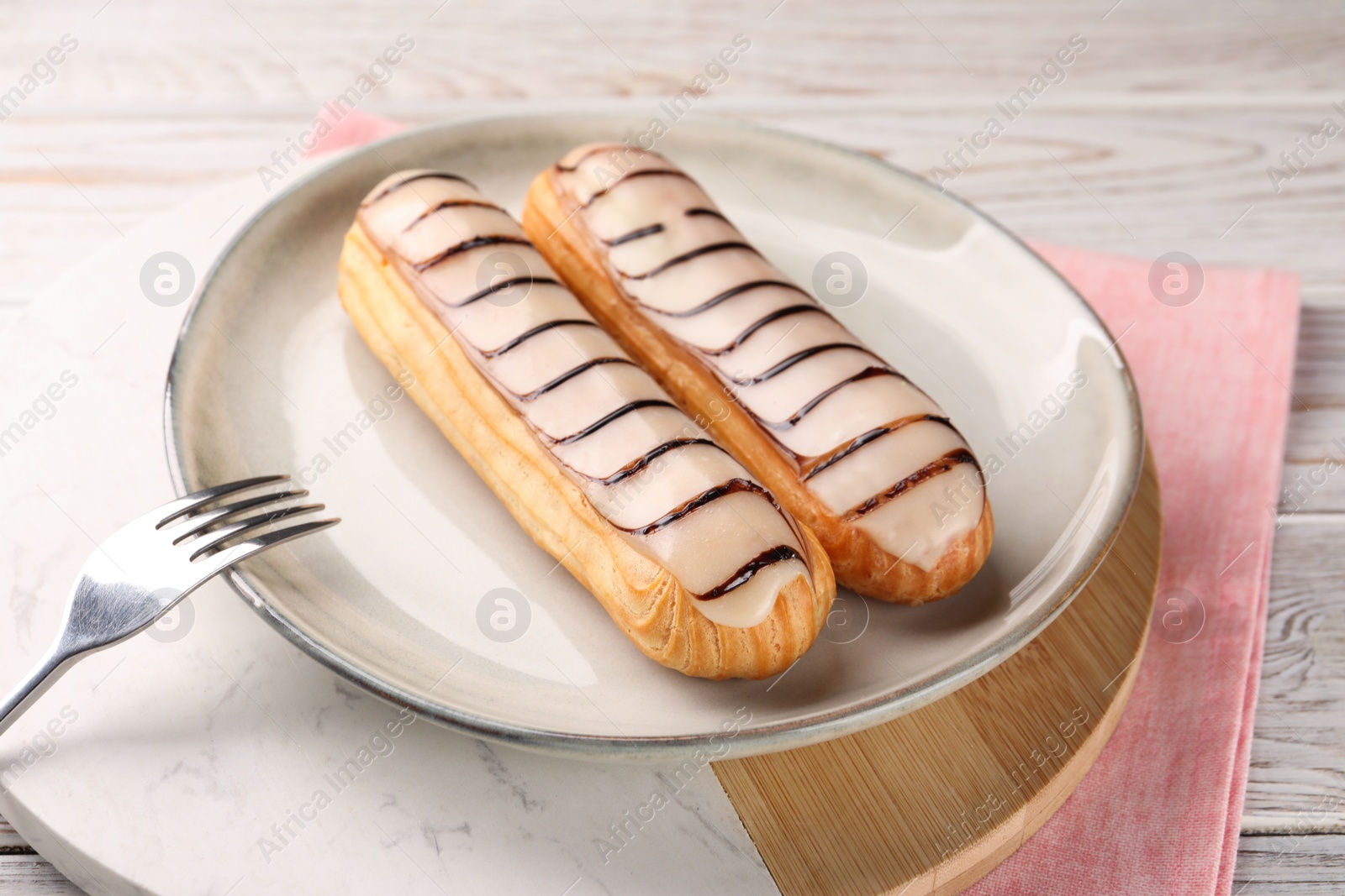 Photo of Tasty glazed eclairs served on wooden rustic table, closeup