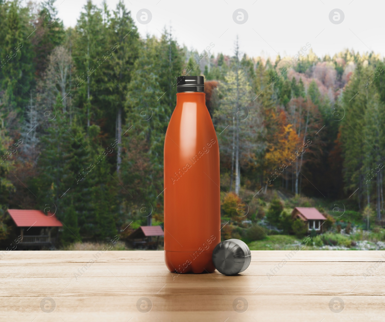 Image of Orange thermos bottle on wooden table against mountain landscape