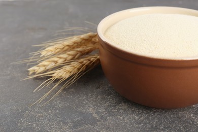 Photo of Semolina in bowl and spikelets on grey table, closeup