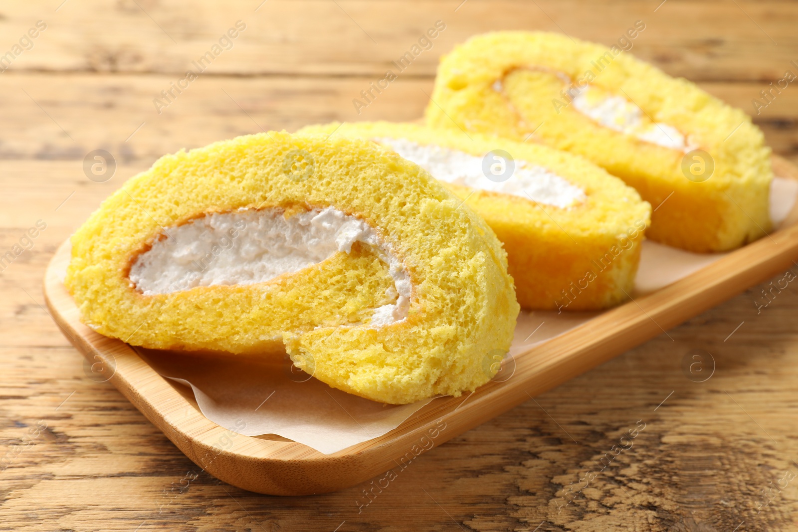 Photo of Delicious cake roll with cream filling on wooden table, closeup