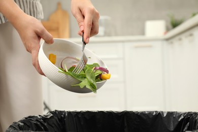 Woman throwing vegetable salad into bin indoors, closeup