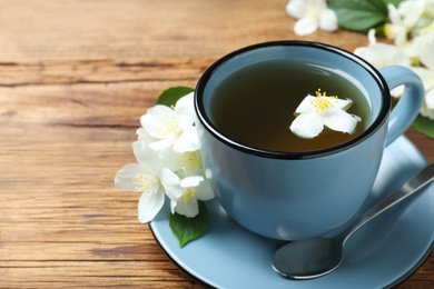 Photo of Cup of tea and fresh jasmine flowers on wooden table