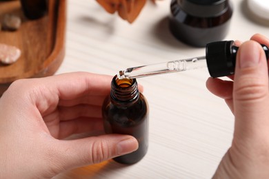 Photo of Woman with bottle of cosmetic serum and pipette at white table, closeup