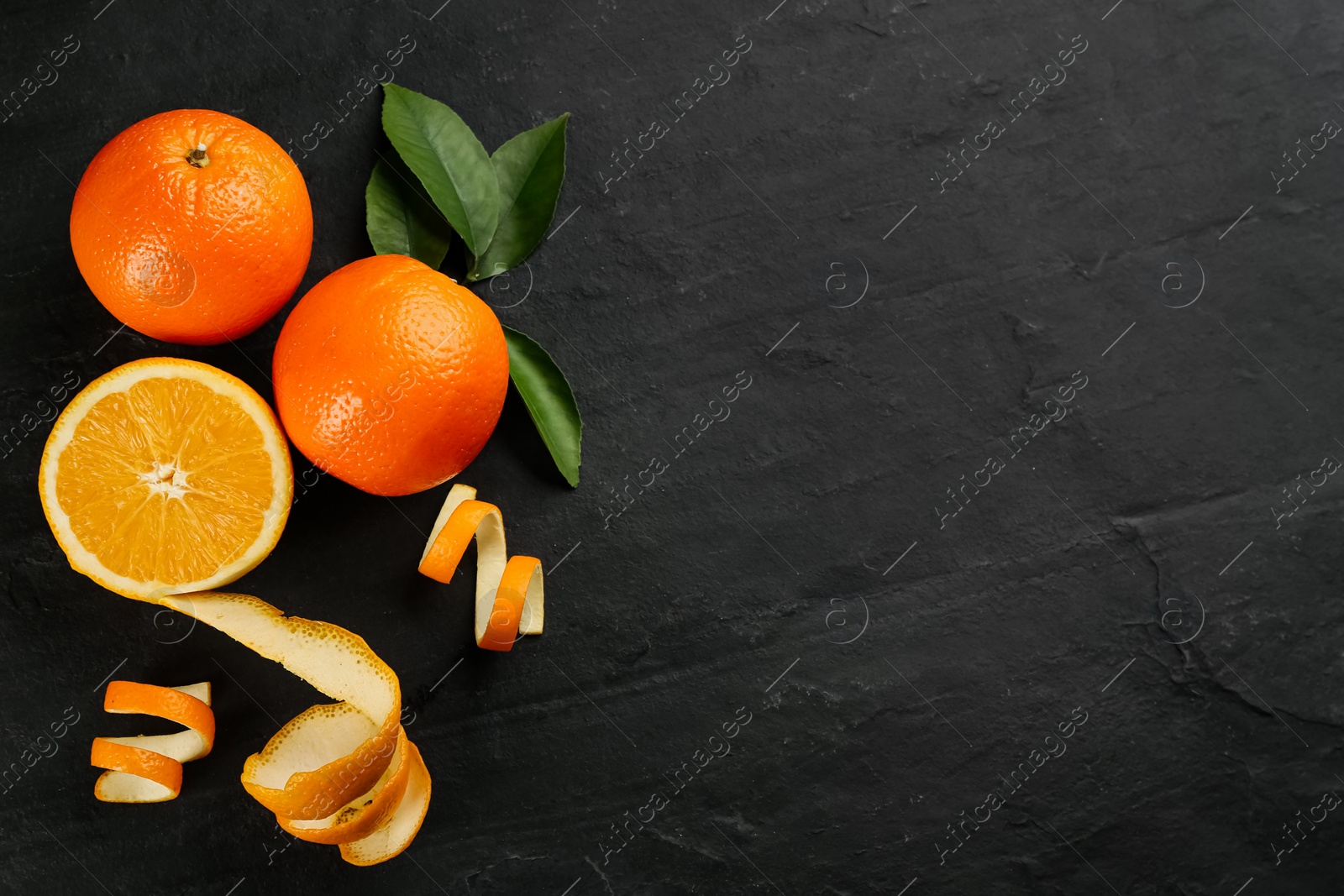 Photo of Orange fruits with peels on black table, flat lay. Space for text