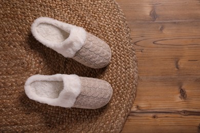 Pair of warm stylish slippers and wicker mat on wooden floor, flat lay. Space for text