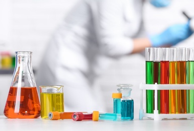 Photo of Different glassware on table and scientist in chemistry laboratory