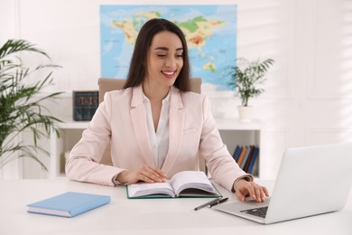 Happy manager working with laptop at desk in travel agency