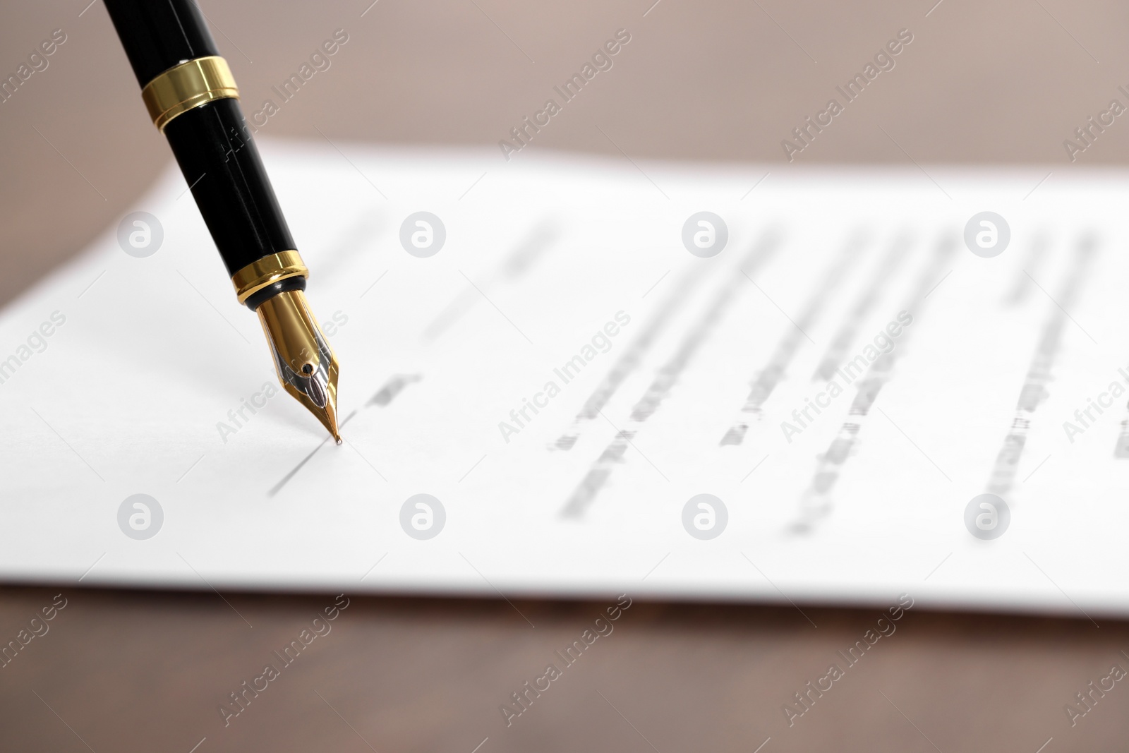 Photo of Writing on document with fountain pen at wooden table, closeup. Notary contract