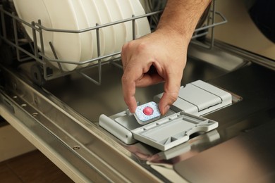 Photo of Man putting detergent tablet into open dishwasher, closeup