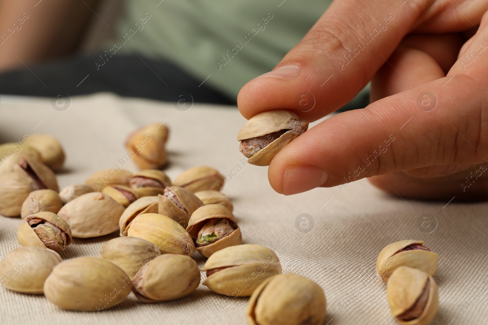 Photo of Woman holding tasty roasted pistachio nut at table, closeup