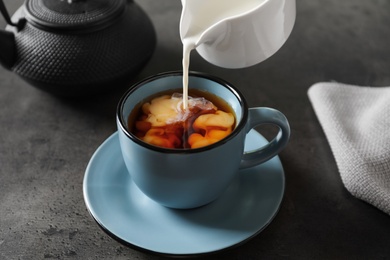 Photo of Pouring milk into cup of black tea on table