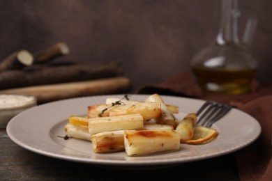 Plate with baked salsify roots, lemon, thyme and fork on wooden table, closeup