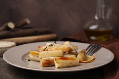 Photo of Plate with baked salsify roots, lemon, thyme and fork on wooden table, closeup