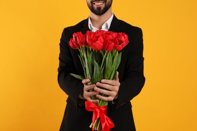 Photo of Happy man with red tulip bouquet on yellow background, closeup. 8th of March celebration