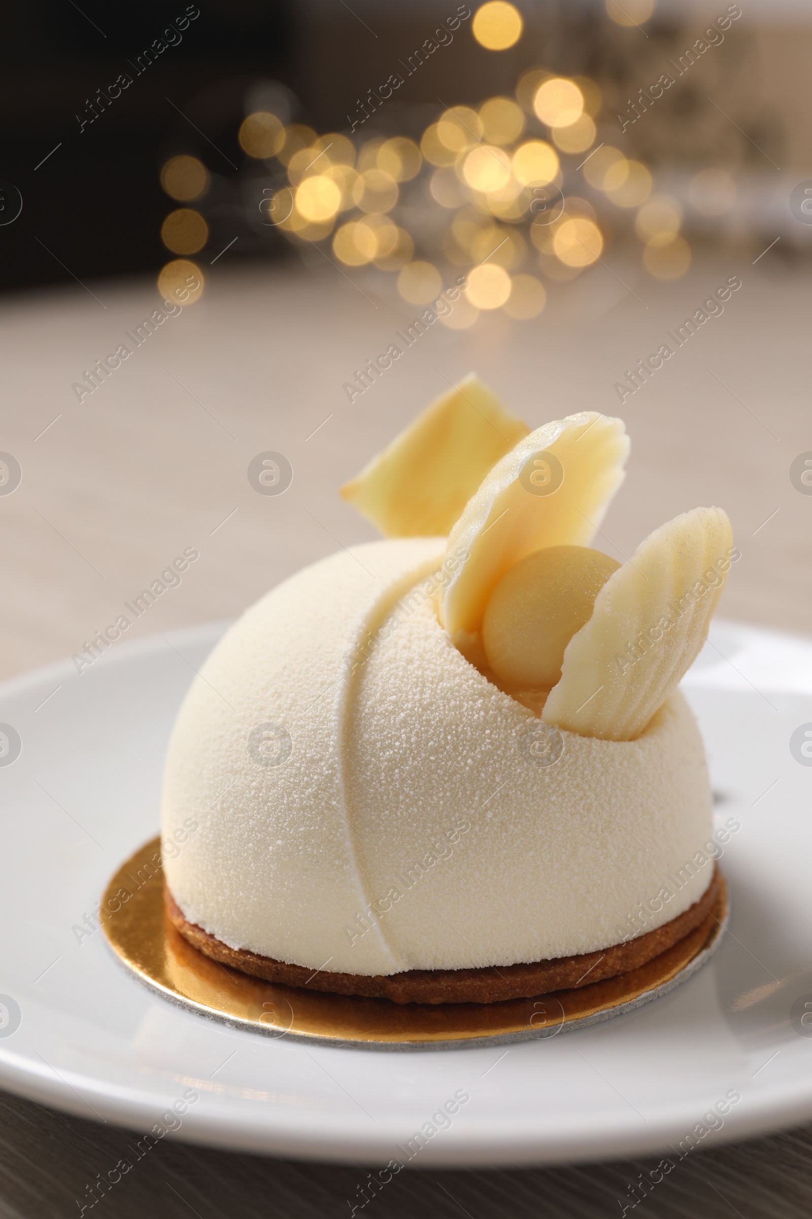 Photo of Delicious mousse cake with white chocolate on plate against blurred lights, closeup