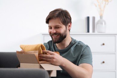 Photo of Happy man opening parcel at home. Internet shopping