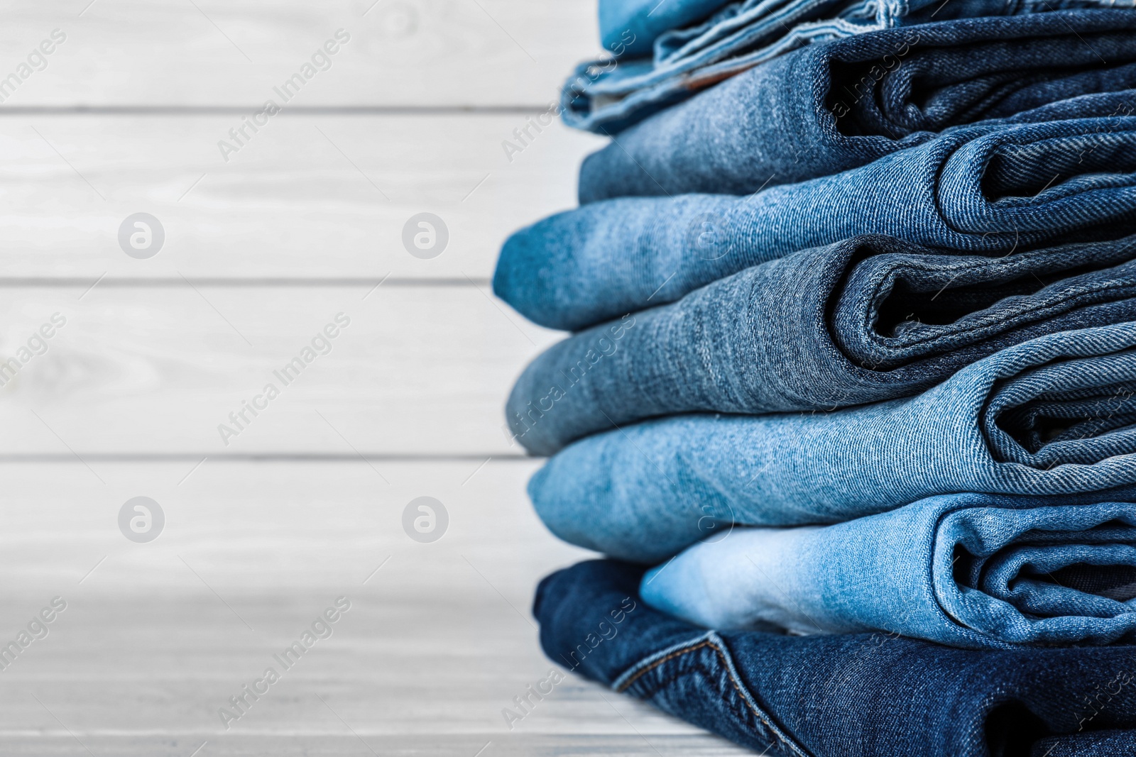 Photo of Stack of different jeans on white wooden table, space for text