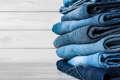 Photo of Stack of different jeans on white wooden table, space for text