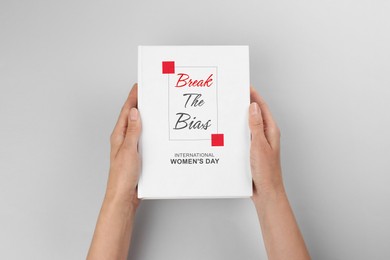 Image of Woman holding book with title Break The Bias devoted to International Women's Day against light grey background, closeup