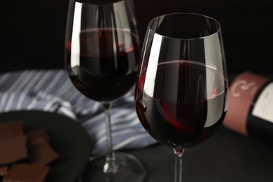 Photo of Glasses of red wine with chocolate on grey table, closeup