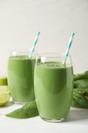 Glasses of healthy green smoothie with fresh spinach on white wooden table against light background