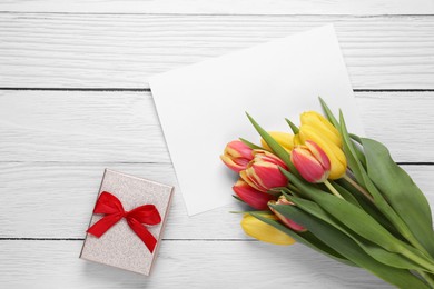 Bouquet of tulips, blank paper sheet and gift box on white wooden table, flat lay. Space for text