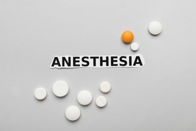 Photo of Word Anesthesia and pills on light grey background, flat lay