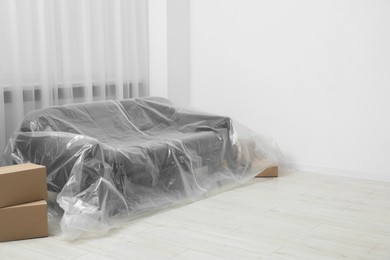 Photo of Stylish sofa covered with plastic film and boxes at home. Space for text