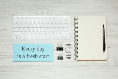 Photo of Note with motivational quote Every day is a fresh start, computer keyboard and office stationery on white wooden background, flat lay