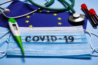 Photo of European Union flag, protective masks and medical items on light blue background. Coronavirus outbreak