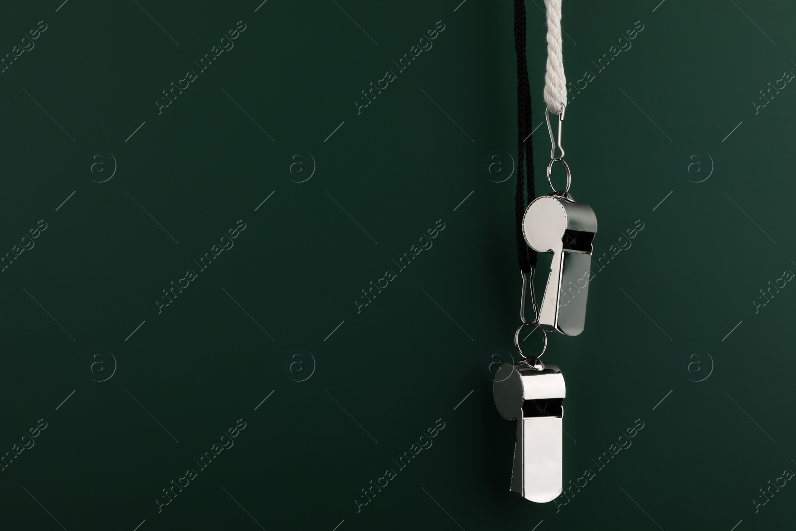 Photo of Referee equipment. Metal whistles on dark green background, closeup and space for text