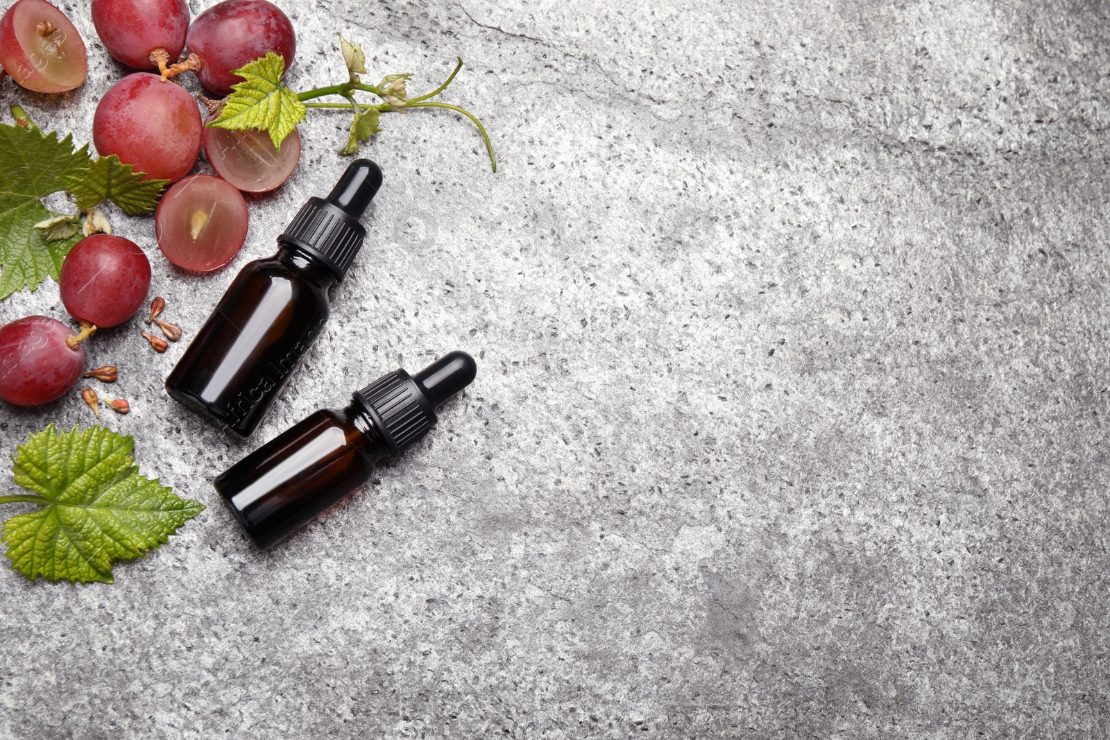 Photo of Bottles of natural grape seed oil on grey table, flat lay with space for text. Organic cosmetic