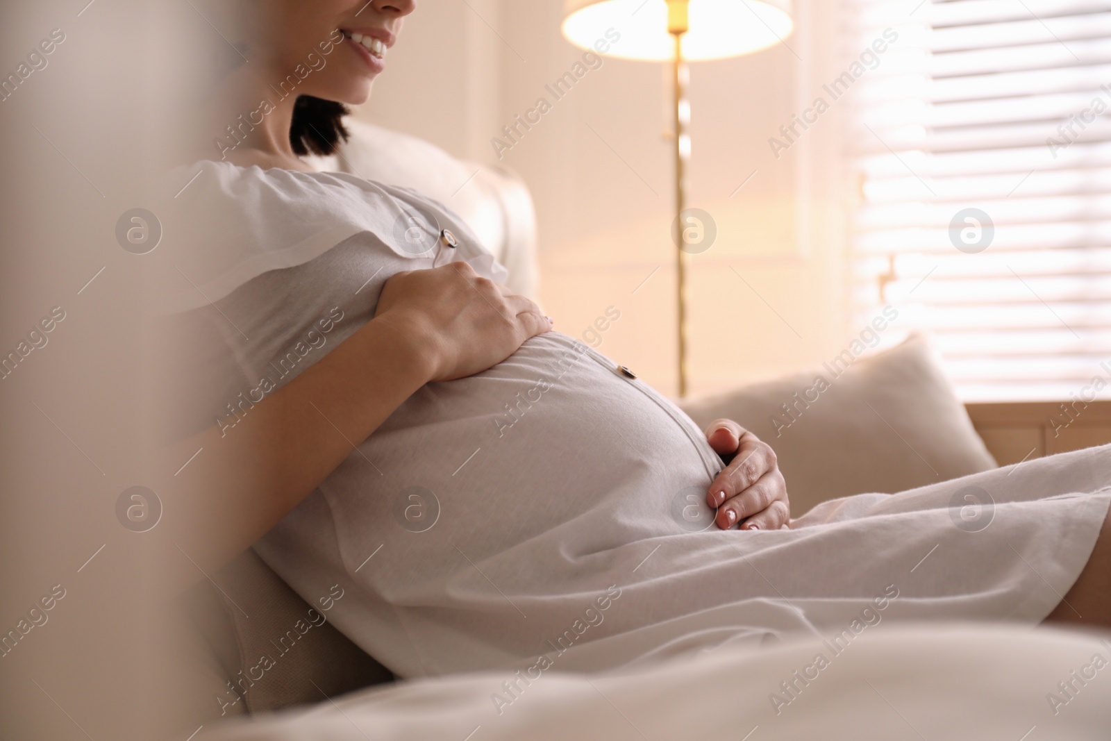 Photo of Pregnant young woman touching belly at home, closeup