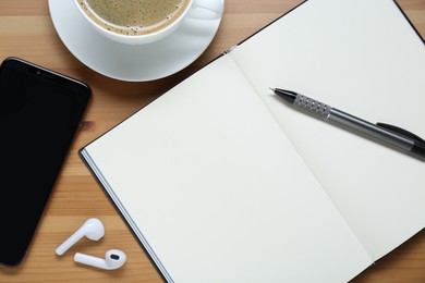 Photo of Empty notebook, smartphone, coffee and stationery on wooden table, flat lay