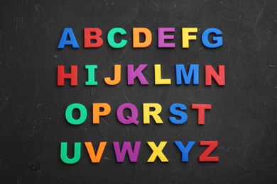 Photo of Colorful magnetic letters on black stone background, flat lay. Alphabetical order