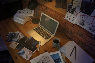 Detective workplace with laptop and documents on wooden table in office