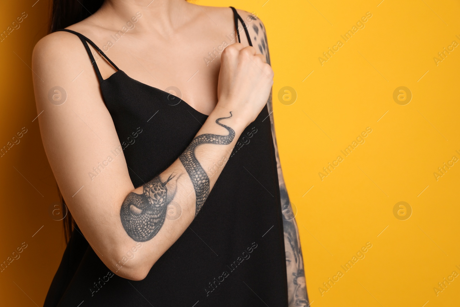 Photo of Beautiful woman with tattoos on arms against yellow background, closeup. Space for text